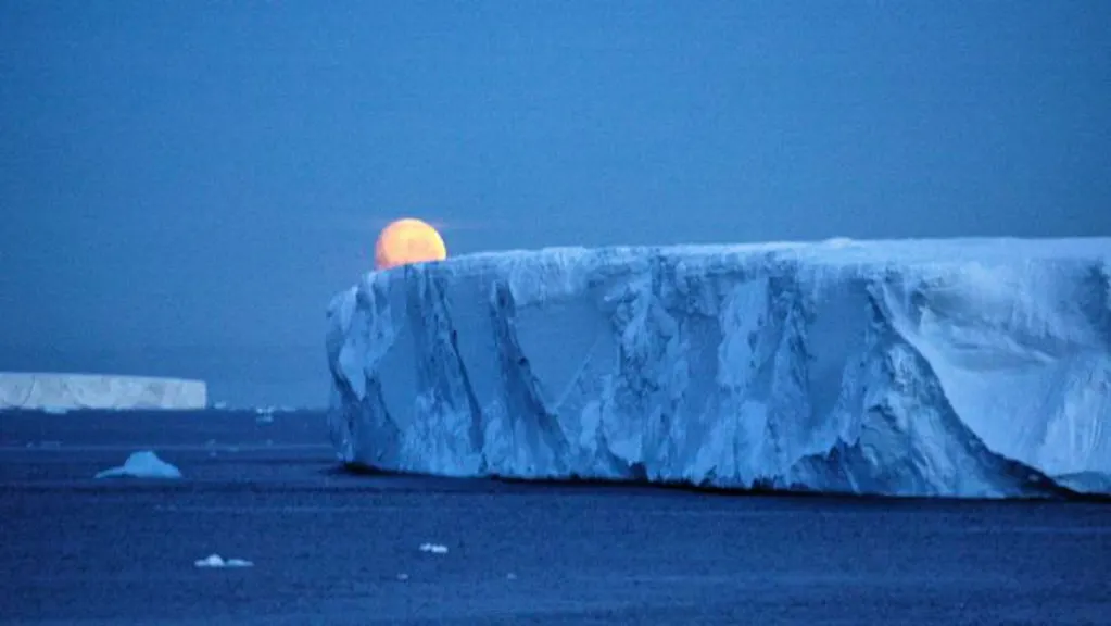 The moon rises over an iceberg in antarctica.
