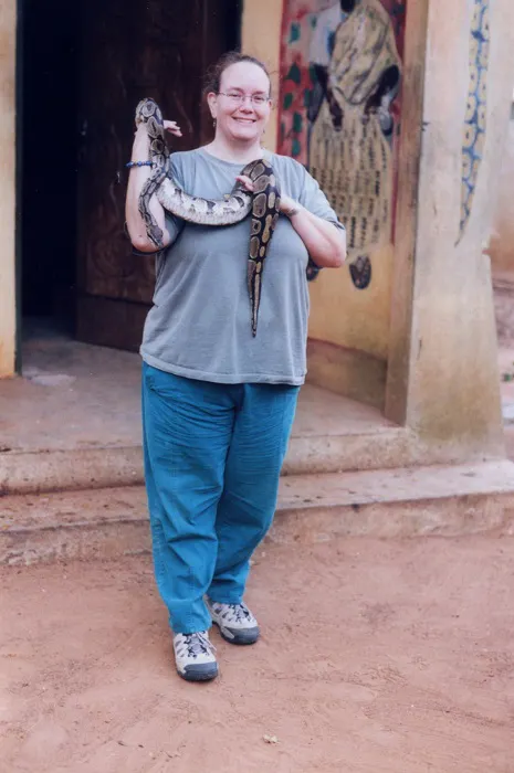 A woman holding a snake in front of a building.