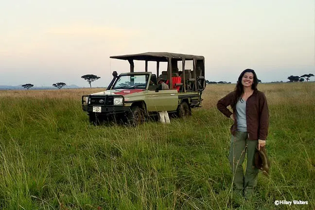 A woman standing next to a jeep in a grassy field.