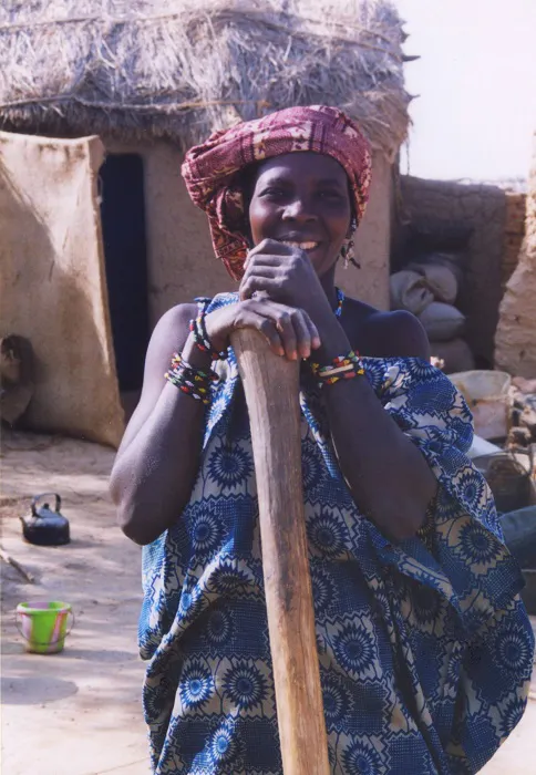 A woman holding a wooden stick in front of a hut.