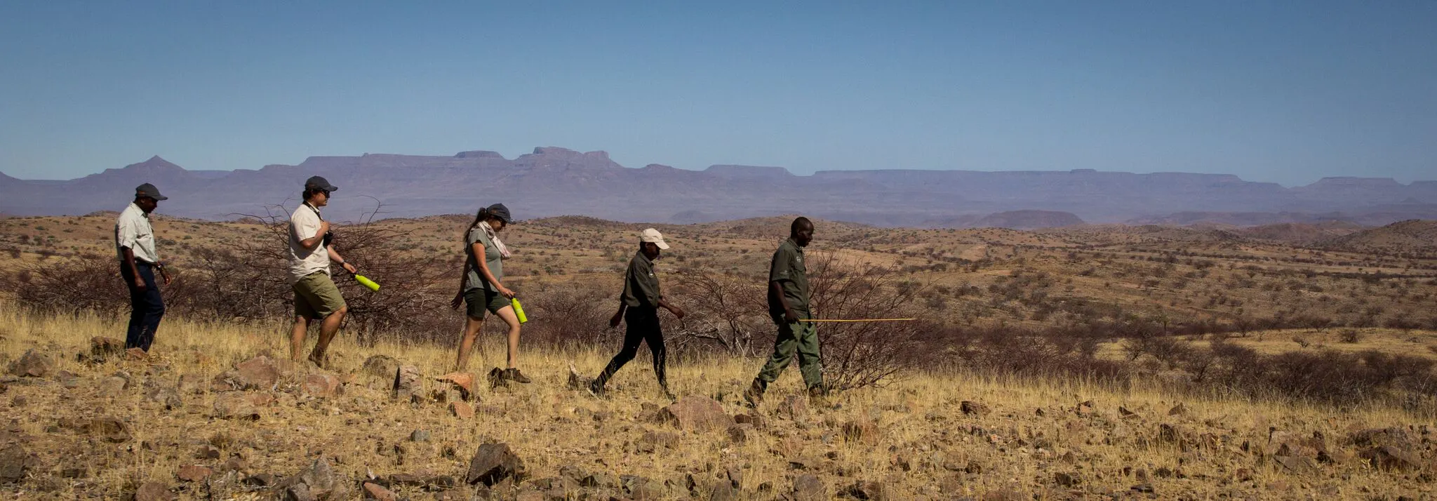 A group of people walking through a desert with mountains in the background.