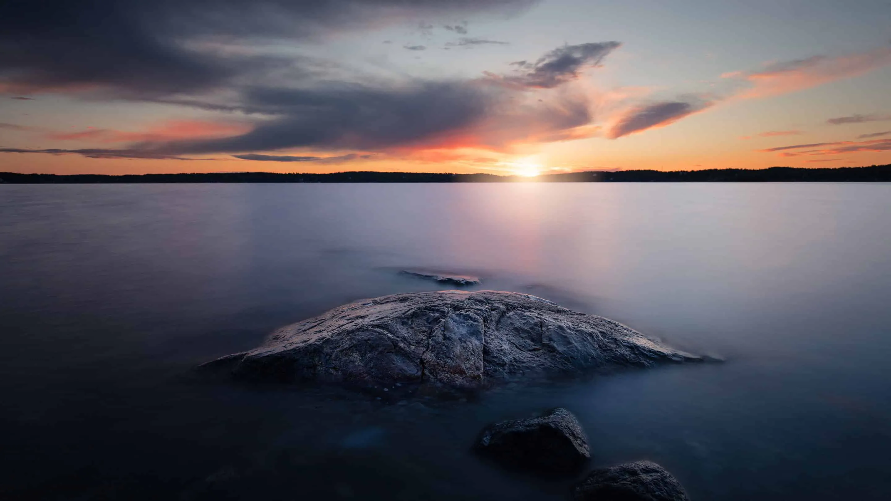 A sunset over a lake with a rock in the water.
