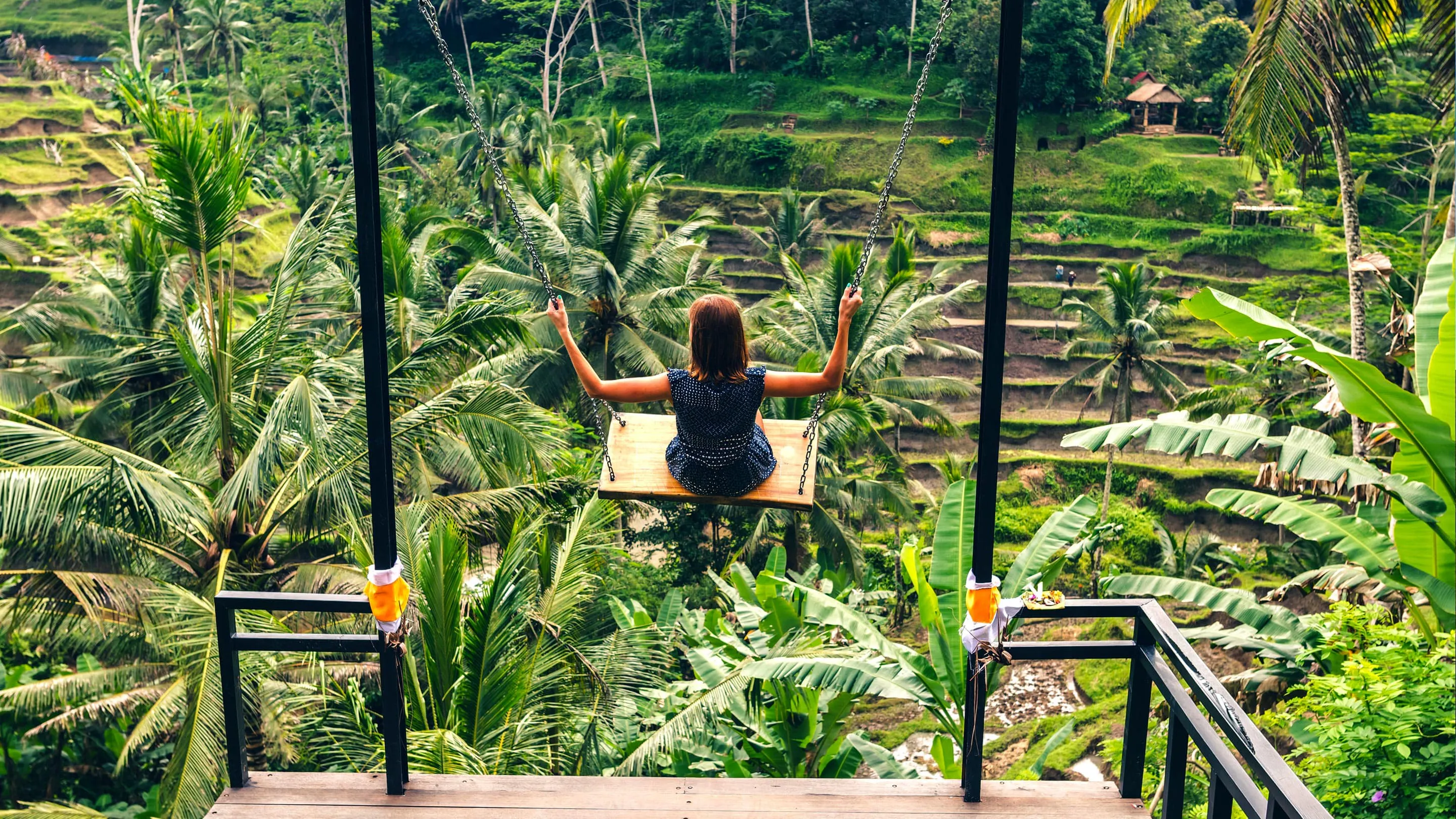 A woman is sitting on a swing in the jungle.