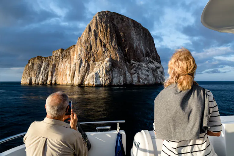 Two people on a boat looking at a rock formation.