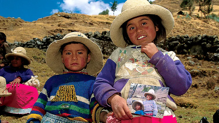 Two children in hats standing on a hillside.