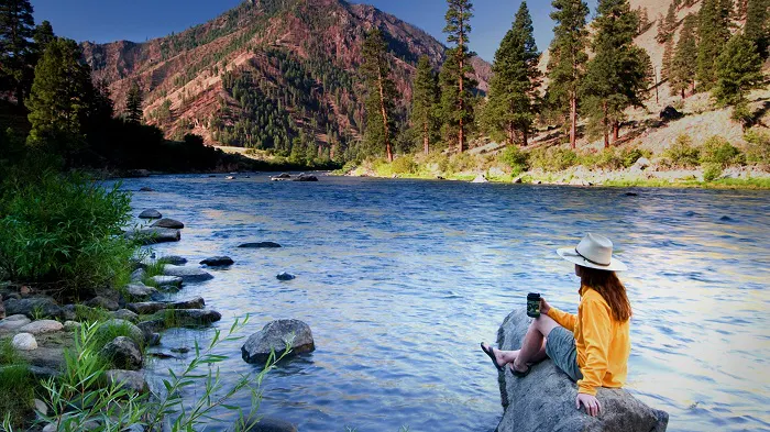 A woman is sitting on a rock near a river.