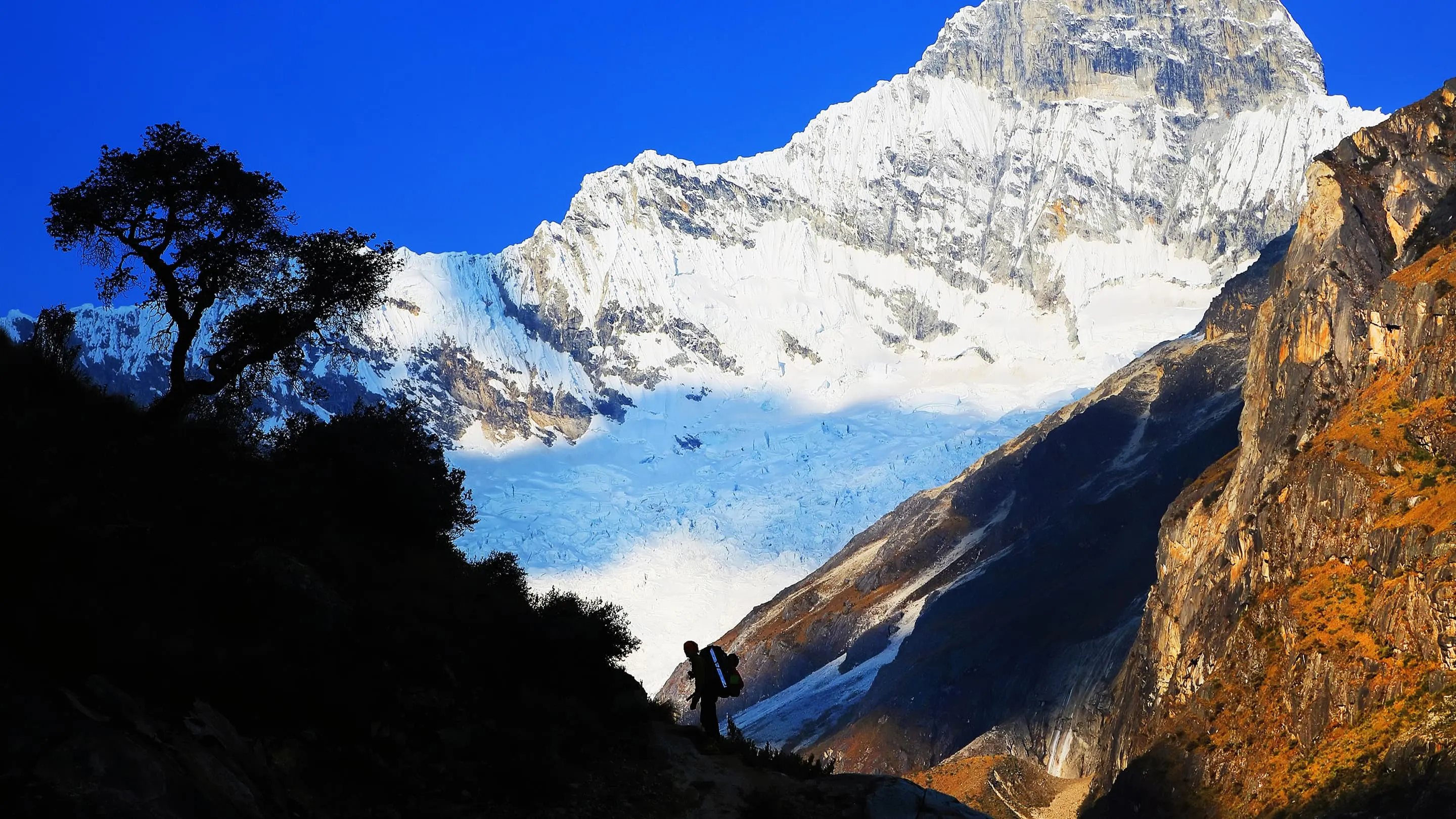 A man is standing next to a mountain with snow on it.