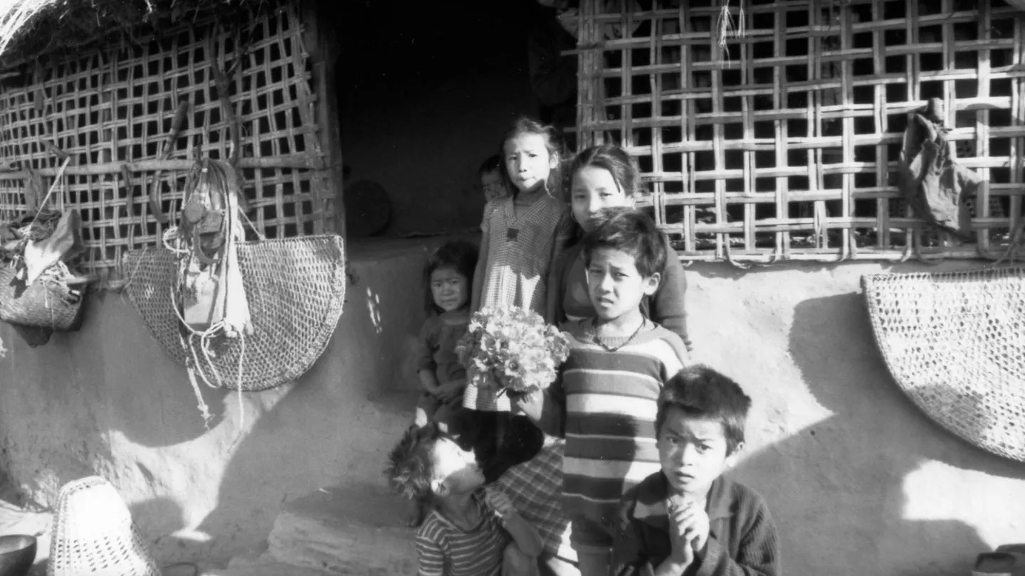 A group of children standing in front of a hut.