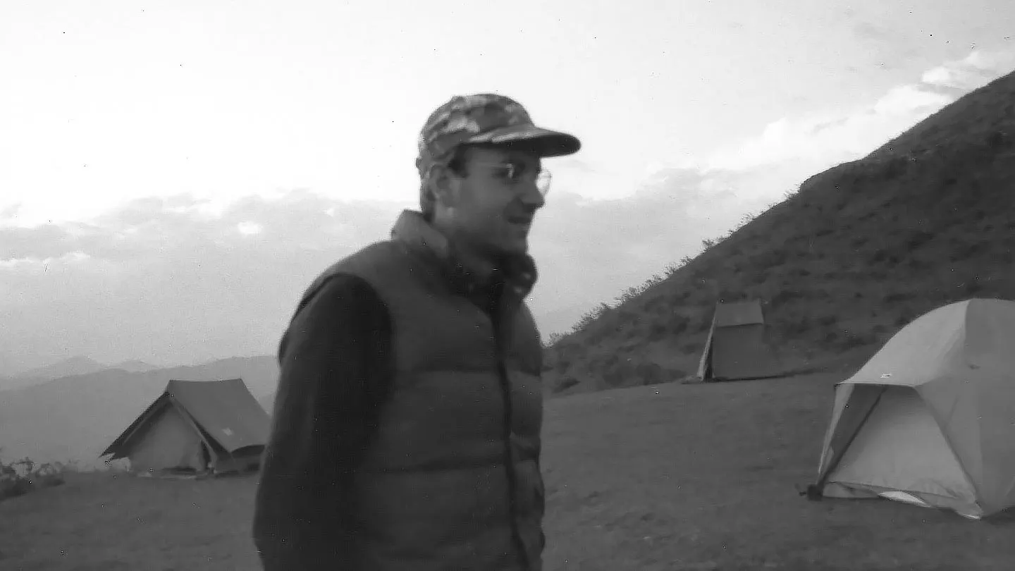 A man standing in front of a tent in the mountains.