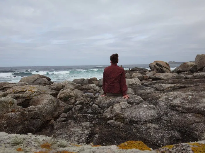 A man sitting on a rock overlooking the ocean.