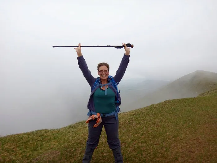 A woman standing on top of a mountain with her arms raised.