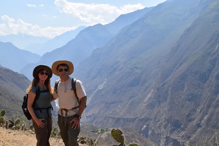 Two people standing in front of a mountain with cactus in the background.