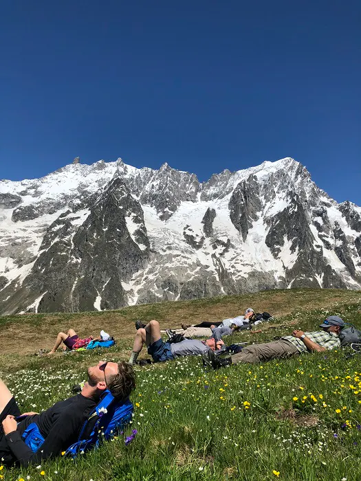 A group of people laying in the grass with mountains in the background.