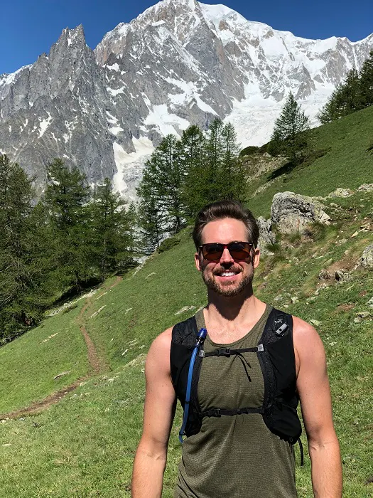 A man standing in front of a mountain with a backpack.