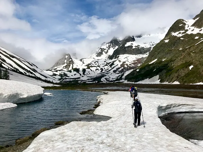 A group of people walking through a snowy area with mountains in the background.