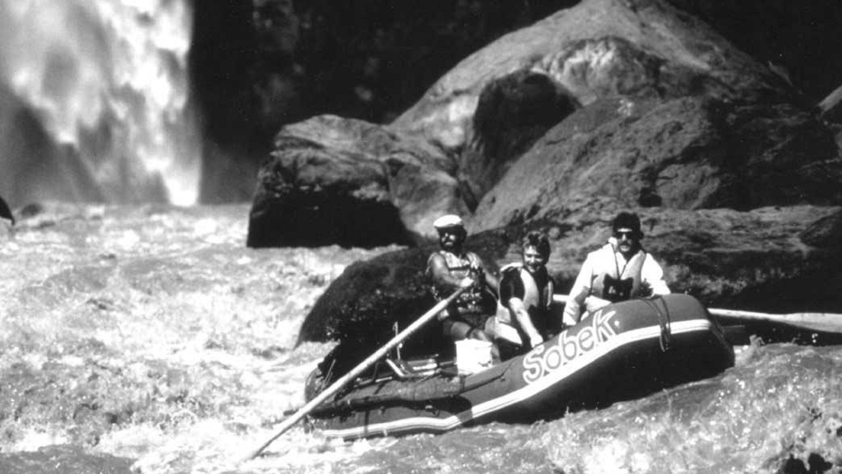 A group of people rafting down a river near a waterfall.