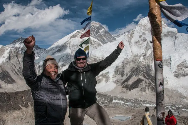 Two men standing on top of a mountain with flags.