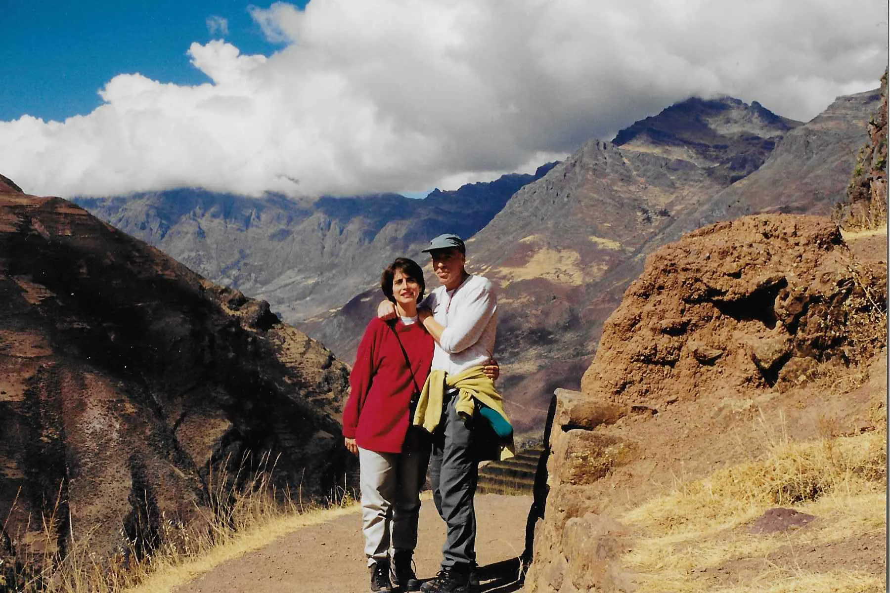 A man and woman standing on a path in the mountains.