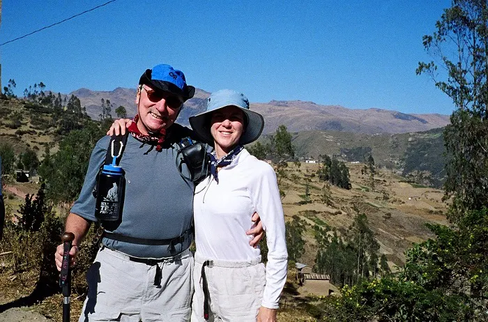 A man and woman standing on a trail with mountains in the background.