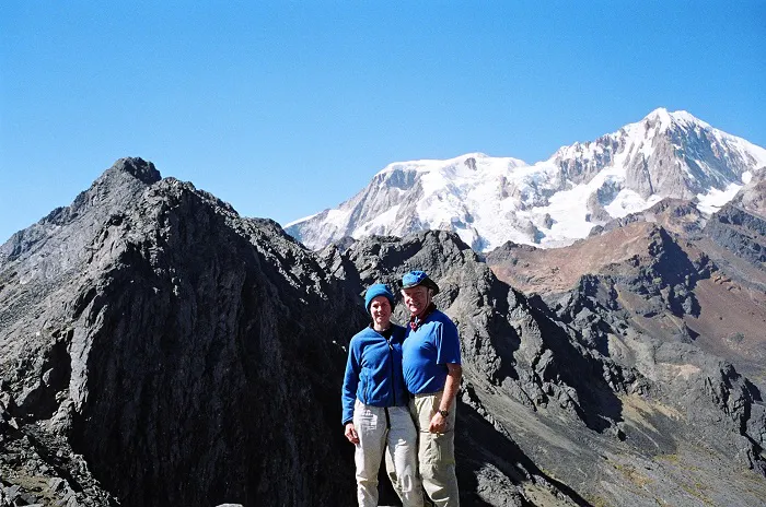 Two people standing on top of a mountain with mountains in the background.