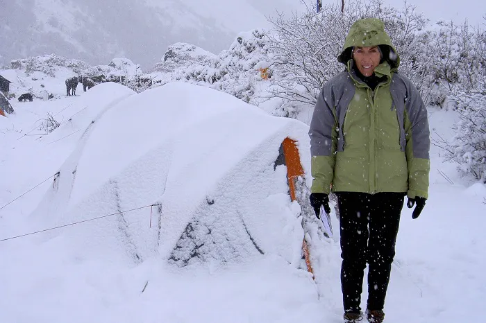 A woman standing in front of a tent covered in snow.