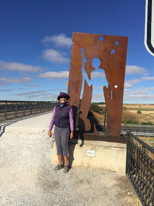 A woman standing next to a metal sculpture on a road.