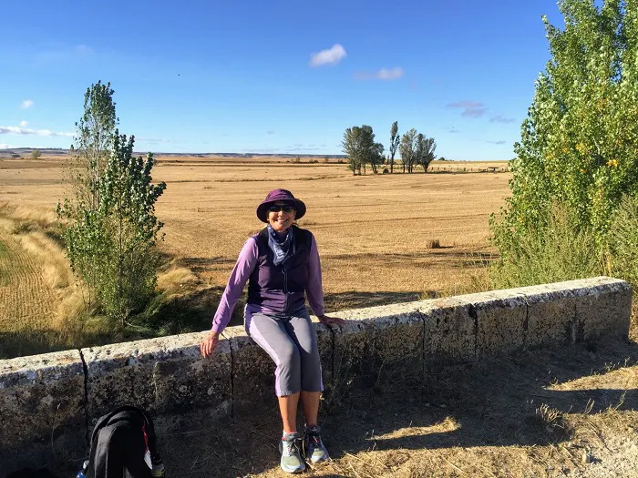 A woman sitting on a wall in front of a field.