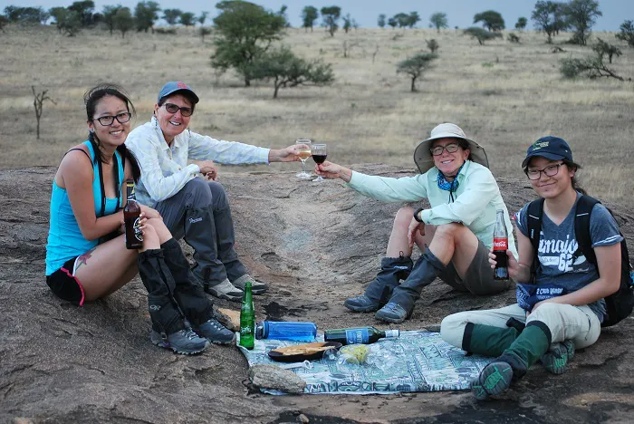 Four women sitting on a rock and drinking wine.