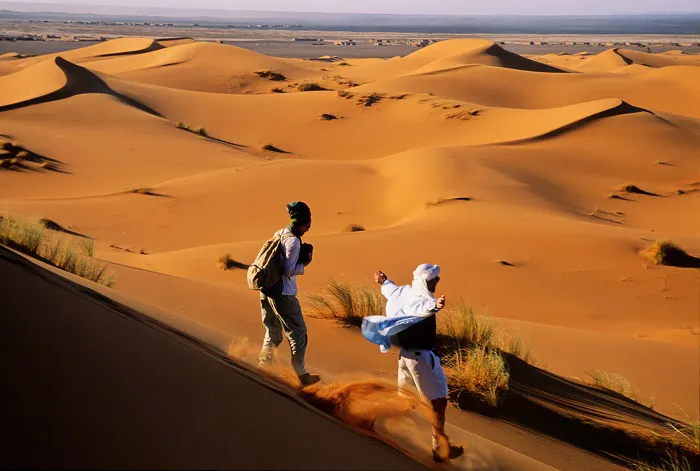 Two people walking through the sahara desert.