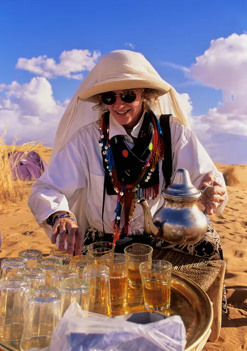 A woman in a hat is making tea in the desert.