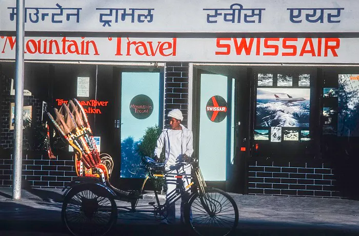 A man with a bicycle in front of a swiss mountain travel store.