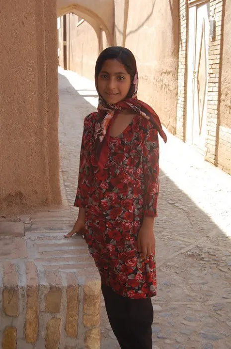 A girl in a red dress standing next to a brick wall.