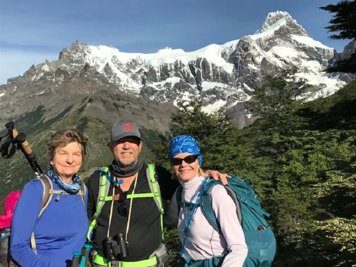 Three people standing in front of a mountain with mountains in the background.