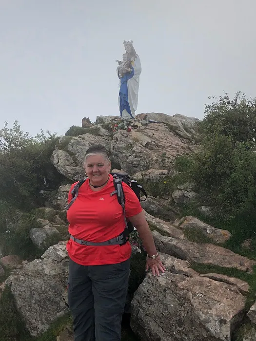 A woman standing on top of a mountain with a statue of jesus.