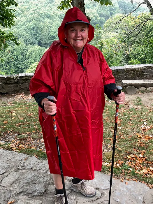 A woman wearing a red raincoat and hiking poles.