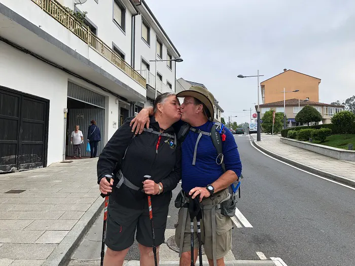 Two people kissing on a street with hiking poles.