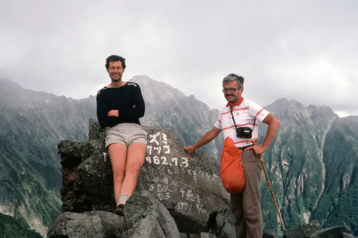 Two men standing on top of a mountain with a sign.
