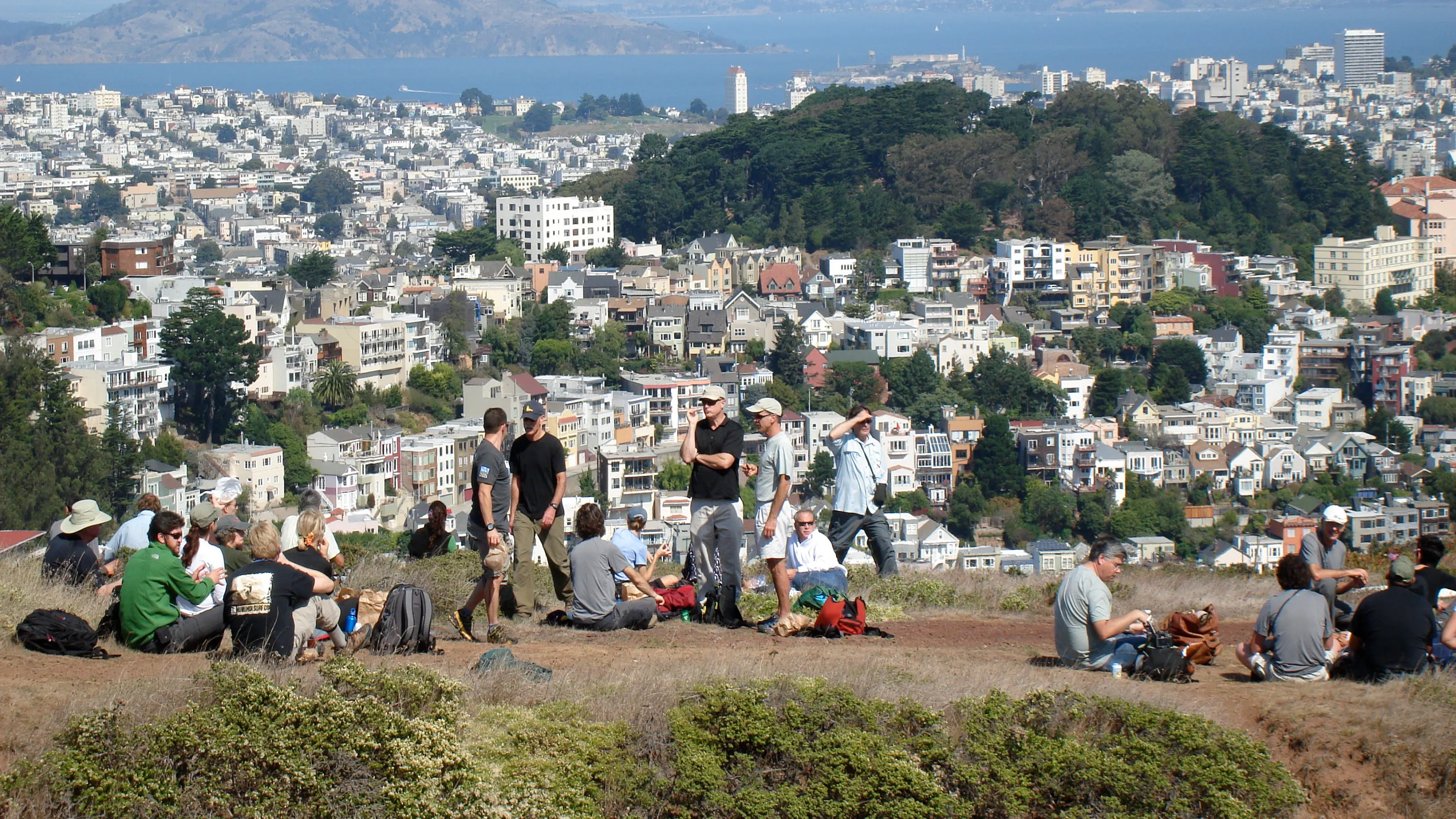 A group of people sitting on a hill overlooking a city.