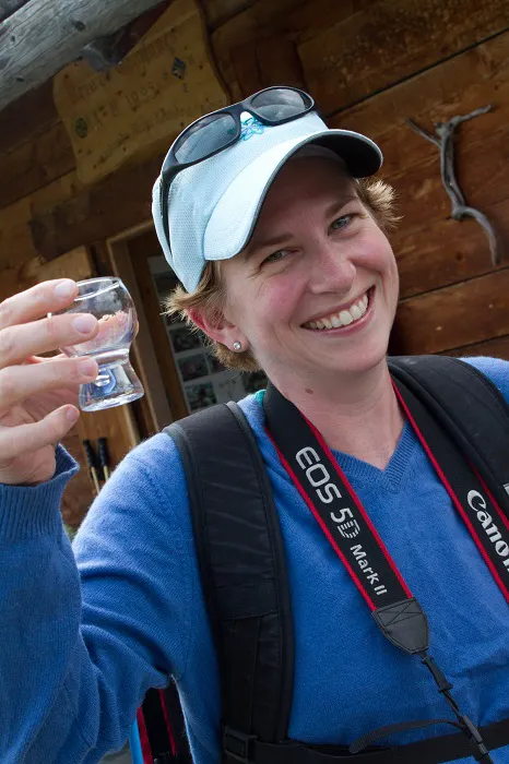 A woman holding a glass of water in front of a cabin.