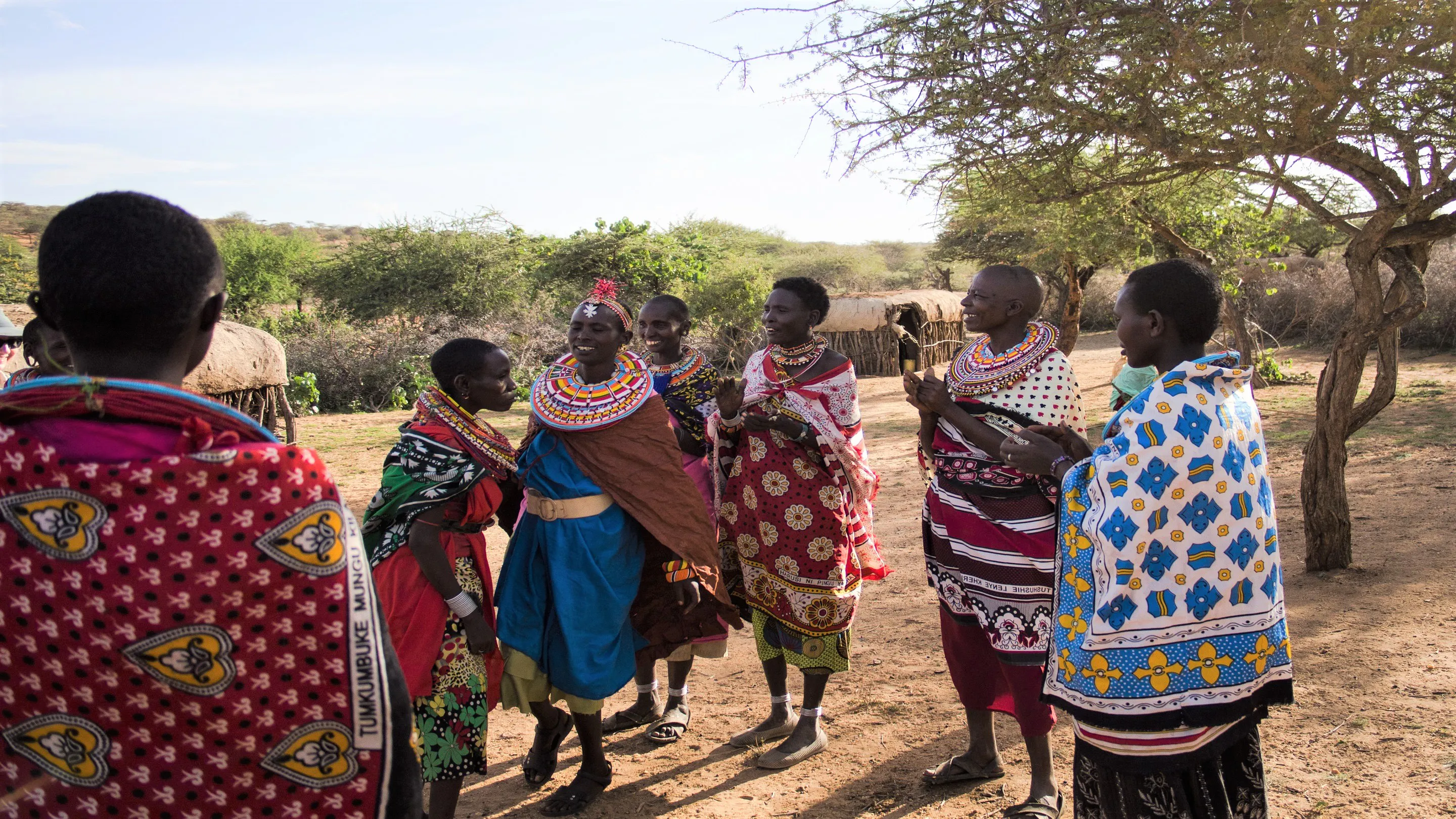 A group of people in traditional clothing standing in a dirt field.