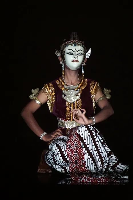 A dancer in a dark room with a mask on her face.