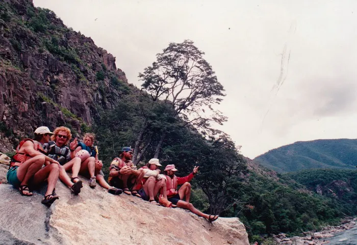 A group of people sitting on a rock next to a river.