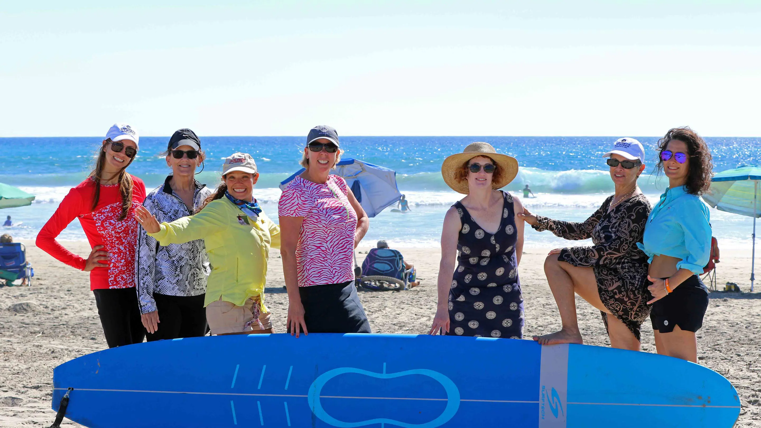 A group of women posing with a surfboard on a beach.