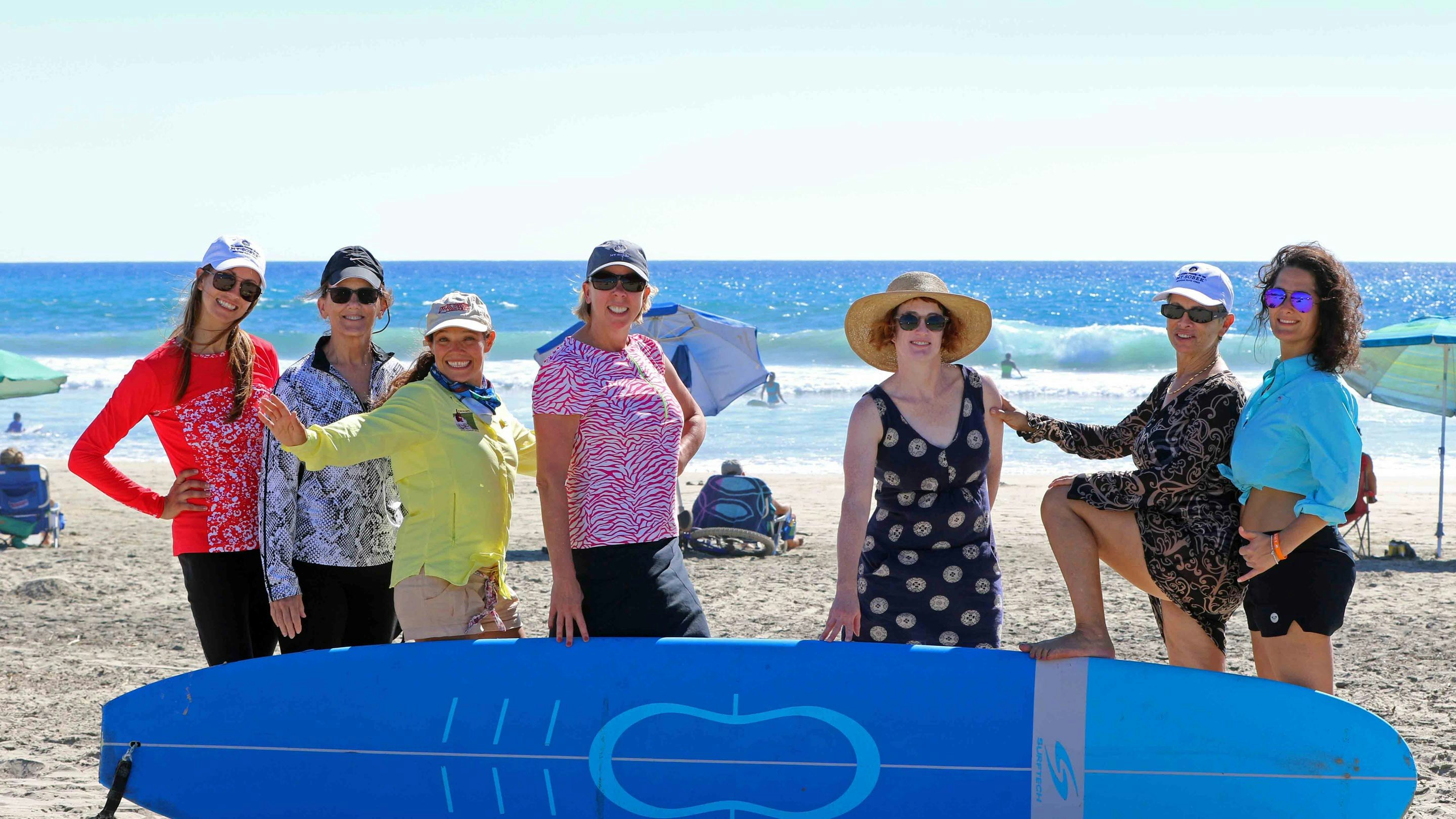 A group of women posing with a surfboard on a beach.