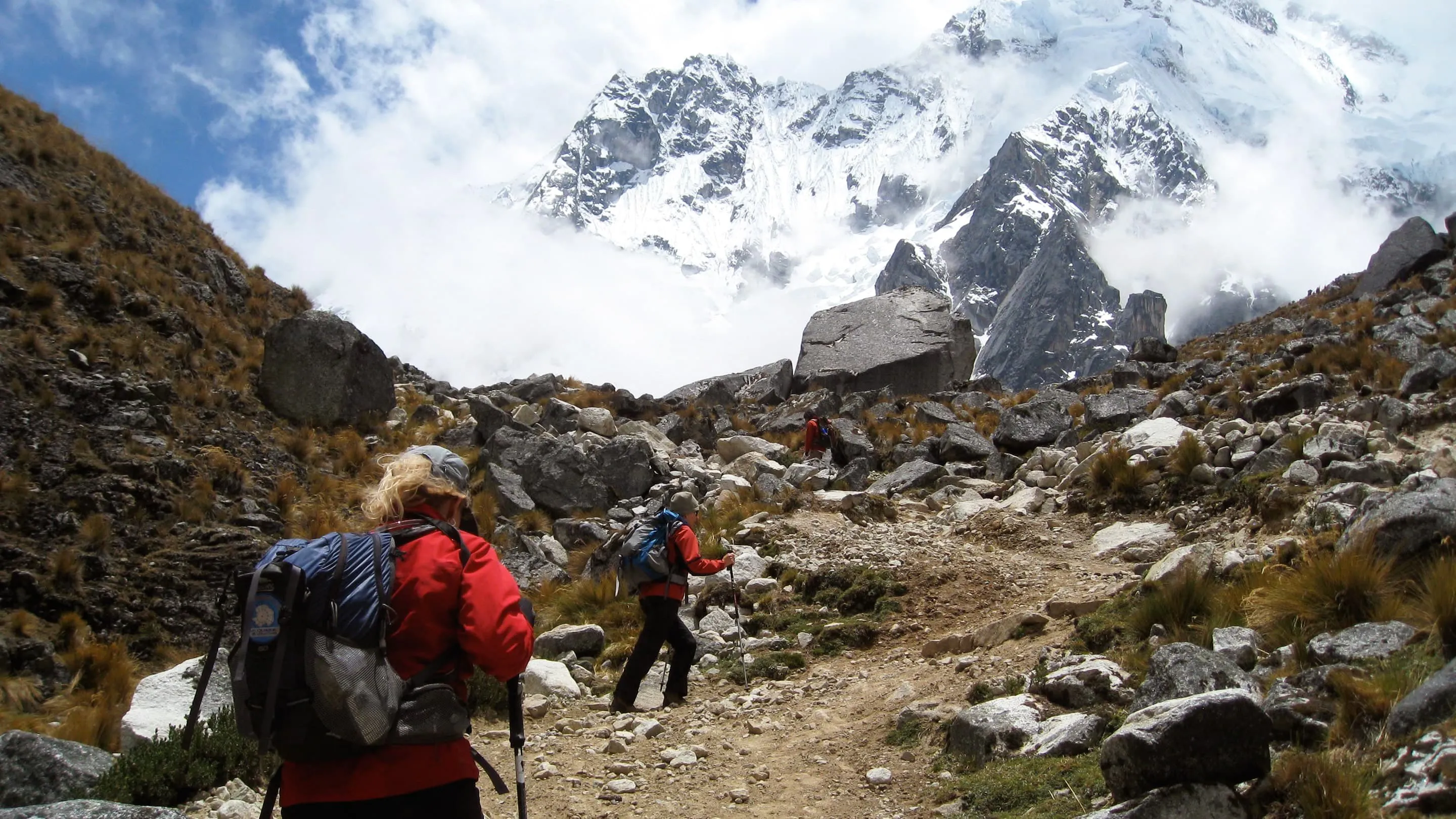 A group of people hiking up a rocky trail with mountains in the background.
