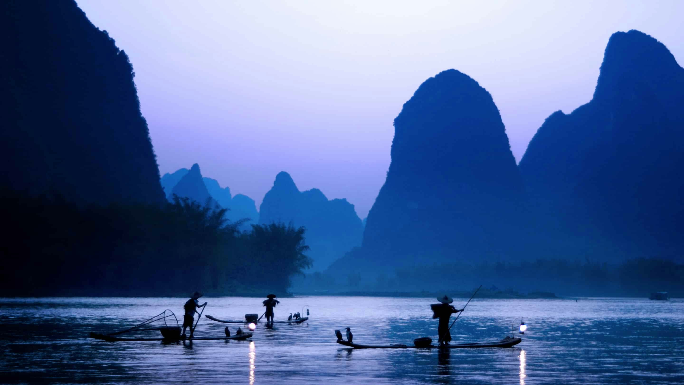 A group of people fishing in a river near mountains.