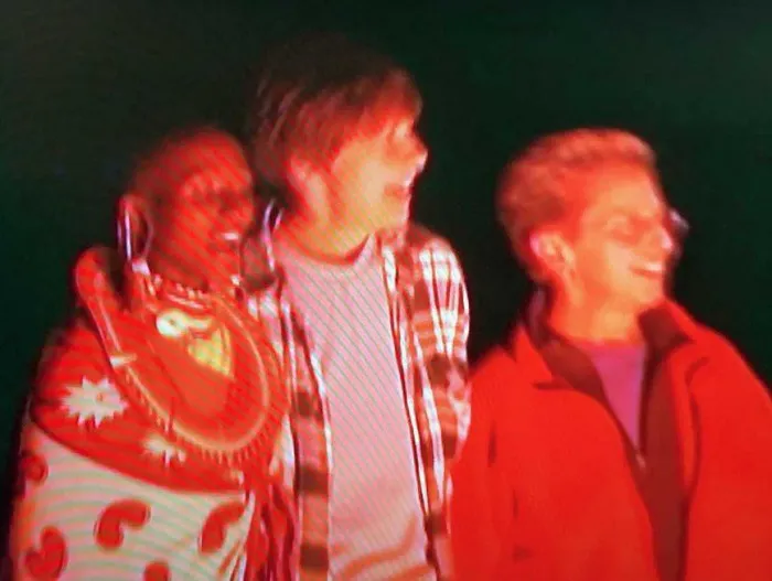 Three people standing next to each other in front of a red light.