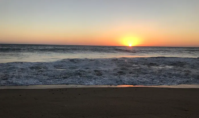 The sun is setting over the ocean on a beach.