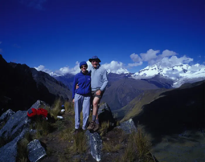 Two people standing on top of a mountain with mountains in the background.