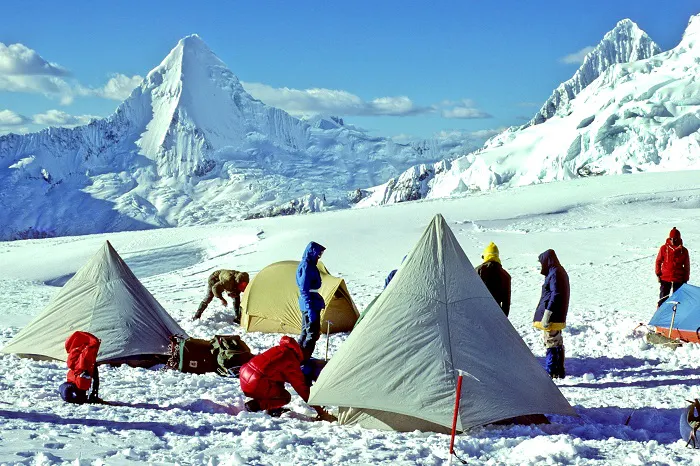 A group of people setting up tents near a snow covered mountain.